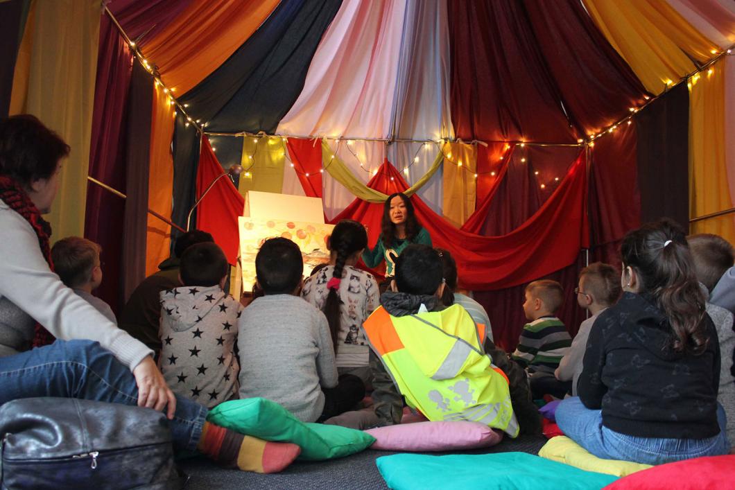 Kinder sitzen unter dem Zelt auf Kissen und lauschen der Märchenerzählerin